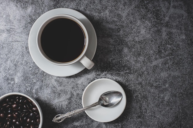 Coffee, white cup and coffee beans, black stone background, top view