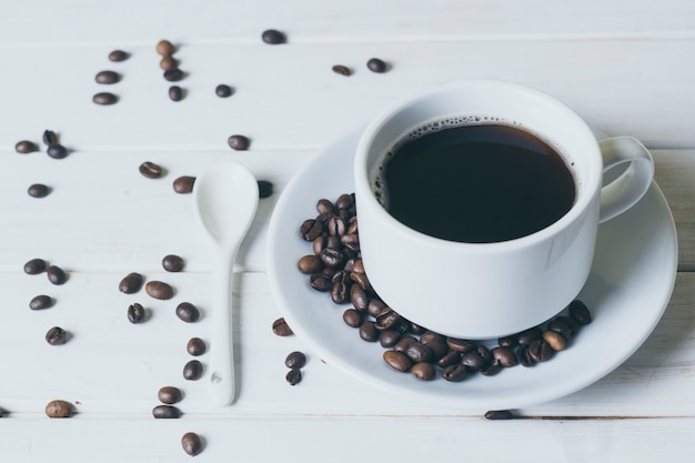 Coffee in a white cup and saucer. Spilled coffee beans, spoon.