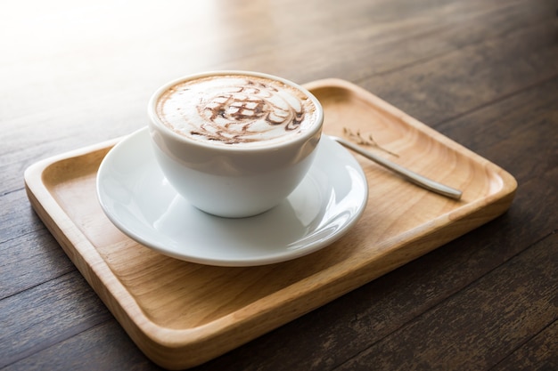 Coffee white cup with beautiful art pattern in wooden tray whute spoon on table. Select focus