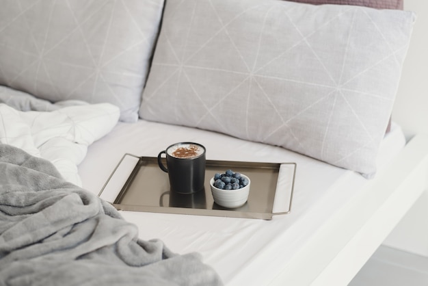 Coffee with cinnamon powder and fresh blueberry on metal tray served in bed