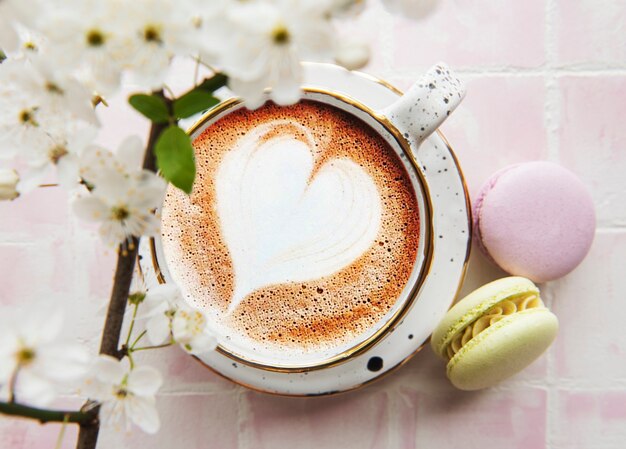 Coffee with a heart-shaped pattern and sweet macaroons desserts on a pink tile background