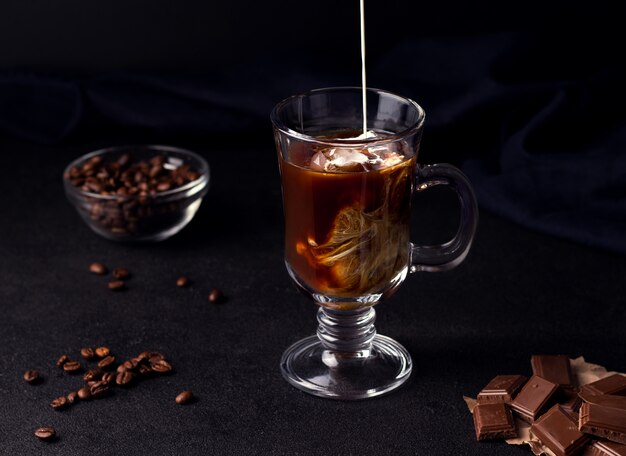 Coffee with ice and cream on a black background next to coffee beans and chocolate