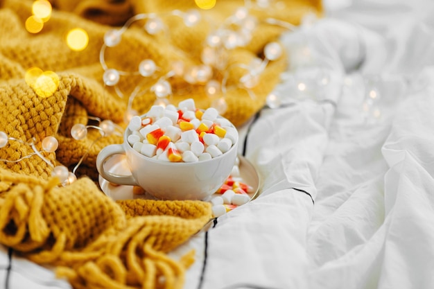 Coffee with marshmallow and candy corn on bed with warm plaid. Autumn beverage, Breakfast in bed. Hygge concept.