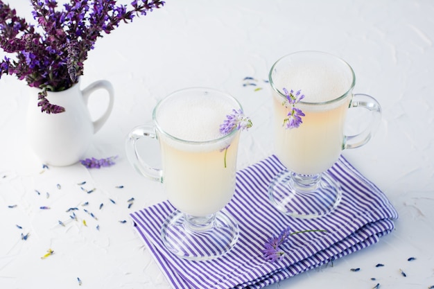 Coffee with milk, foam and lavender in glasses and a bouquet of flowers in a jug on a white table. Copy space