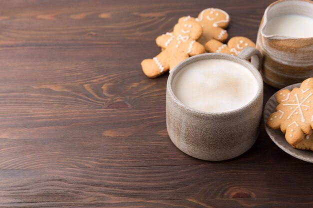 木製の背景にミルクとジンジャーブレッドのクッキーとコーヒー。冬のホットドリンク。