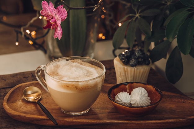 カフェでの朝食用のコーヒー、ミルク、メレンゲ、ベリーのケーキ。木製のテーブルと蘭