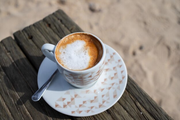 Coffee with milk on wooden table in sand