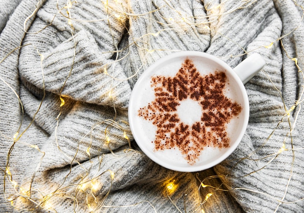 Coffee with a snowflake pattern on a warm knitted sweater surface