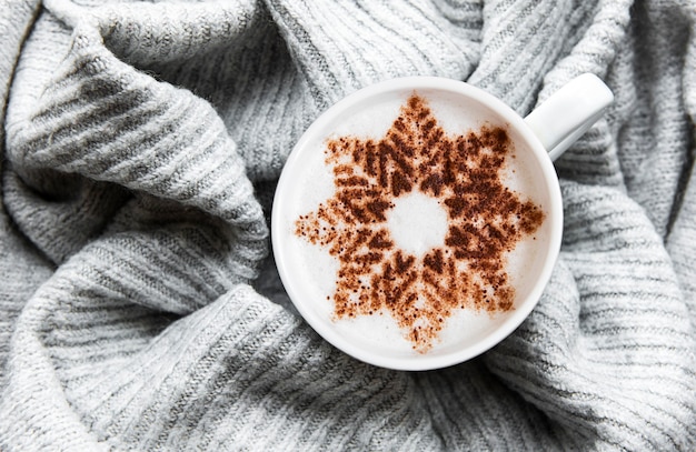 Caffè con un motivo a fiocco di neve su una calda superficie del maglione lavorato a maglia