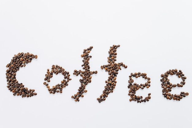 Кофейное слово написано на кофейных зернах на белом фоне