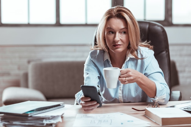 Coffee at work. Beautiful stylish lawyer feeling relieved and relaxed drinking some coffee at work