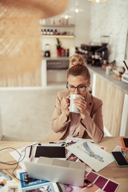 仕事中のコーヒー。彼女のコーヒーを飲み、彼女のスケッチに取り組んでいる美しい思いやりのある女性。