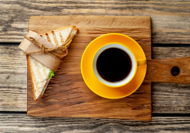 coffee in a yellow mug and sandwich on a cutting board