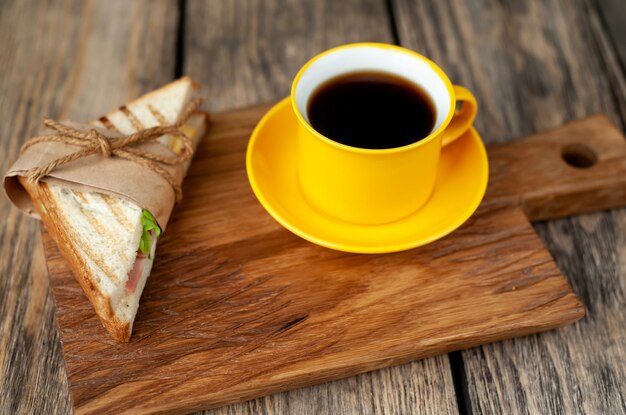 coffee in a yellow mug and sandwich on a cutting board