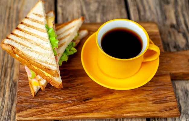 coffee in a yellow mug and sandwiches on a cutting board