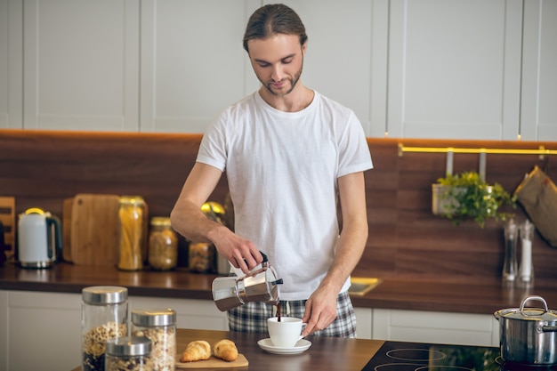 コーヒー。カップにコーヒーを注ぐ家庭用品の若い男