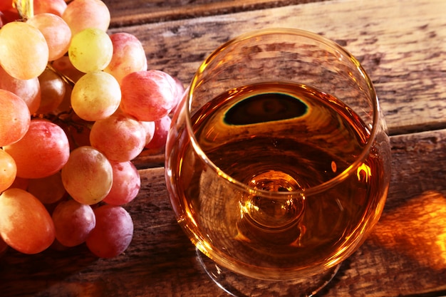 Cognac or Brandy in a glass and fresh grapes, still life in rustic style, vintage wooden background, selective focus.