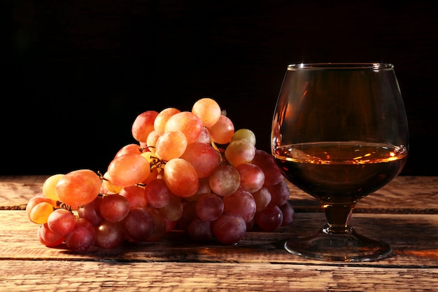 Cognac or Brandy in a glass and fresh grapes, still life in rustic style, vintage wooden background,