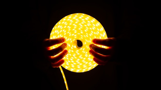 Coil of glowing LED strip with warm light in hand.