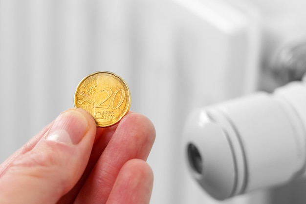 Foto moneta in mano con un termostato del radiatore di riscaldamento il concetto della crisi energetica e il risparmio di denaro dal bilancio familiare