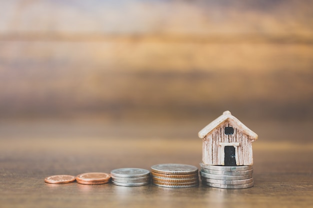 Coin money and house model on wooden background 