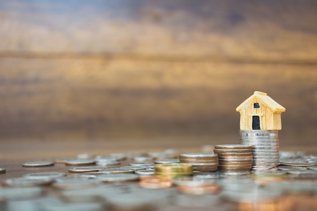 Coin money and house model on wooden background 