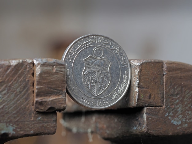 Coin one Tunisian Dinar, clamped in a metal vise