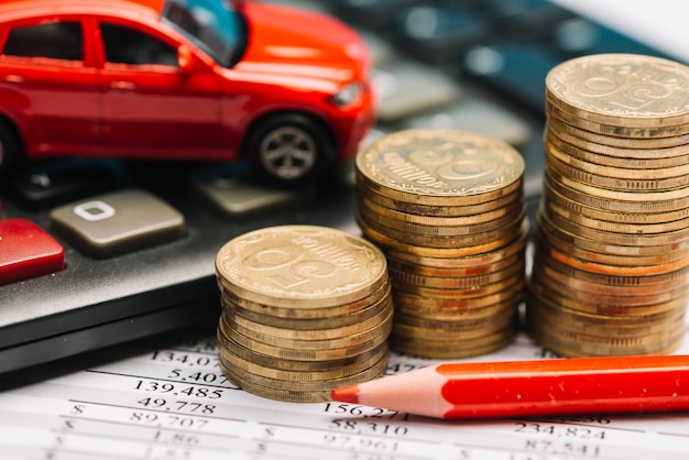 Coin stack; calculator; toy car on financial report with red colored pencil