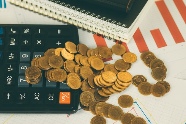 Coin stack and financial graph paper sheet with calculator on table