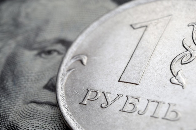 A coin with a face value of 1 ruble lies on a banknote of the American dollar closeup