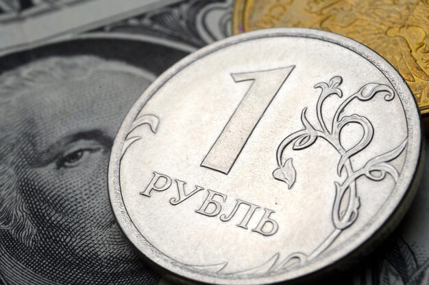 A coin with a face value of 1 ruble lies on a banknote of the American dollar closeup