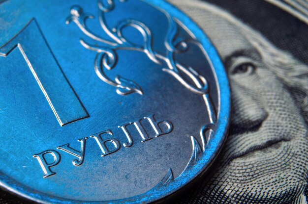 A coin with a face value of 1 ruble lies on a banknote of the American dollar closeup