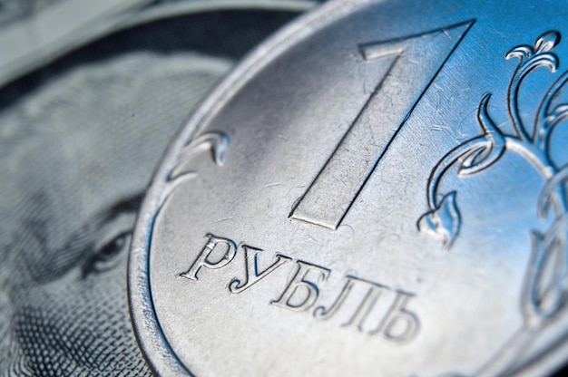 A coin with a face value of 1 ruble lies on a banknote of the American dollar closeup