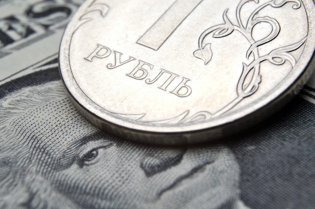 A coin with a face value of 1 ruble lies on a banknote of the American dollar closeup