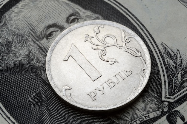 A coin with a face value of 1 ruble lies on a banknote of the American dollar closeup