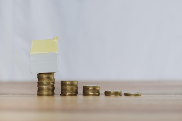 Coins are arranged on a wooden table with a model of a house showing that the interest.