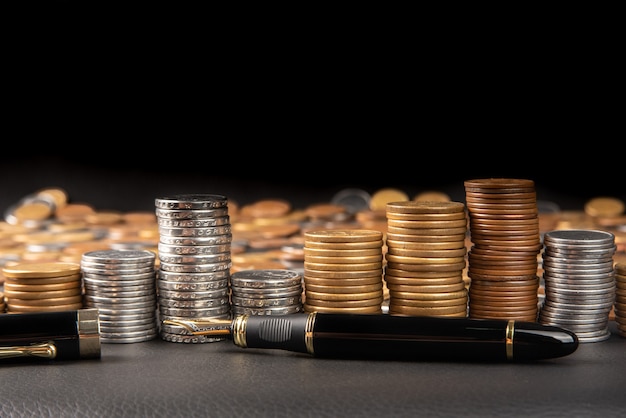 Coins, Brazilian coins of various amounts piled up and a fountain pen on black leather, selective focus.