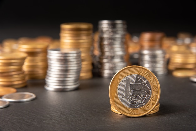 Coins, Brazilian coins of various amounts stacked and a one real coin in the foreground on black leather, selective focus.