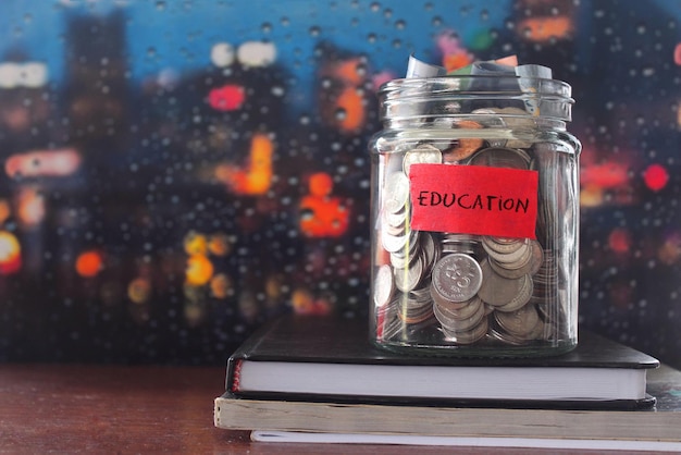 Coins in glass jar label with education and book on wooden table Financial concept