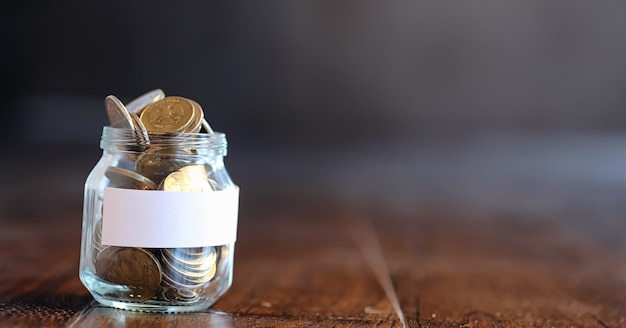 Coins in a glass jar on a wooden floor. Pocket savings from coins in the bank. Piggy bank in a glass jar with coins.