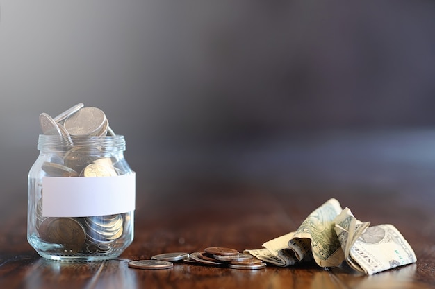 Coins in a glass jar on a wooden floor. Pocket savings from coins in the bank. Piggy bank in glass jar with coins.