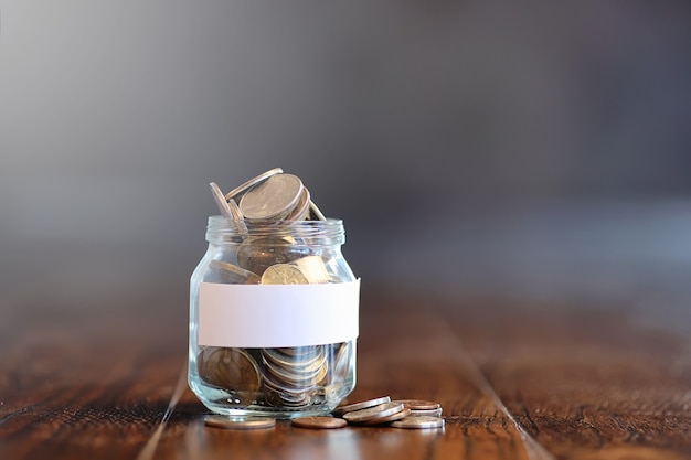 Coins in a glass jar on a wooden floor. Pocket savings from coins in the bank. Piggy bank in glass jar with coins.