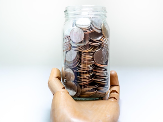 Coins in glass jar on wooden hand isolated on white background