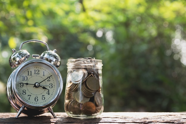 Coins in jar with alarm clock on nature background, Concept finance business