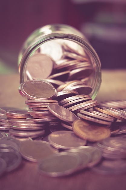 Coins spilling out of a glass bottle with filter effect retro vintage style