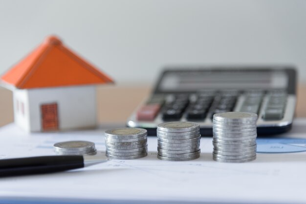 Coins stack with pen, paper house and calculator on business document chart office desk backgrounds