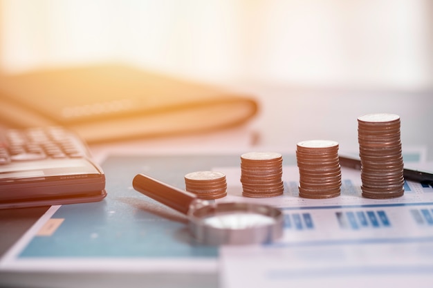 Coins stacking on financial report with magnifier glass and calculator.