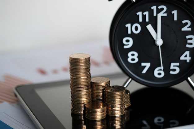 coins stacks and alarm clock with tablet and financial graph paper