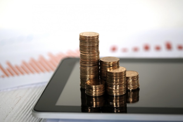 Coins stacks on tablet with financial graph paper.