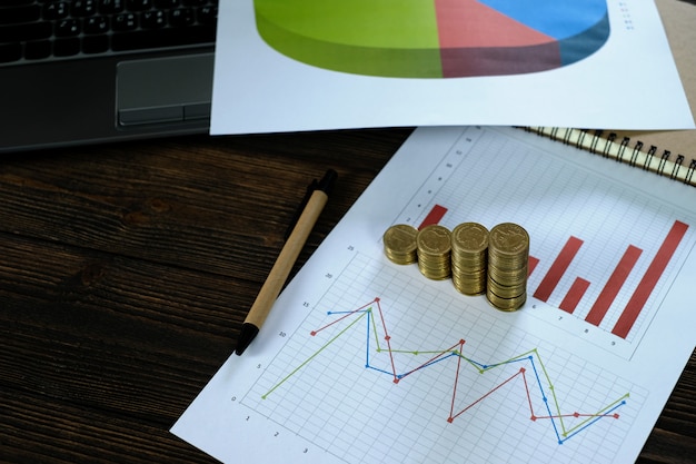 Coins stacks with notebook laptop computer and financial graph on white paper